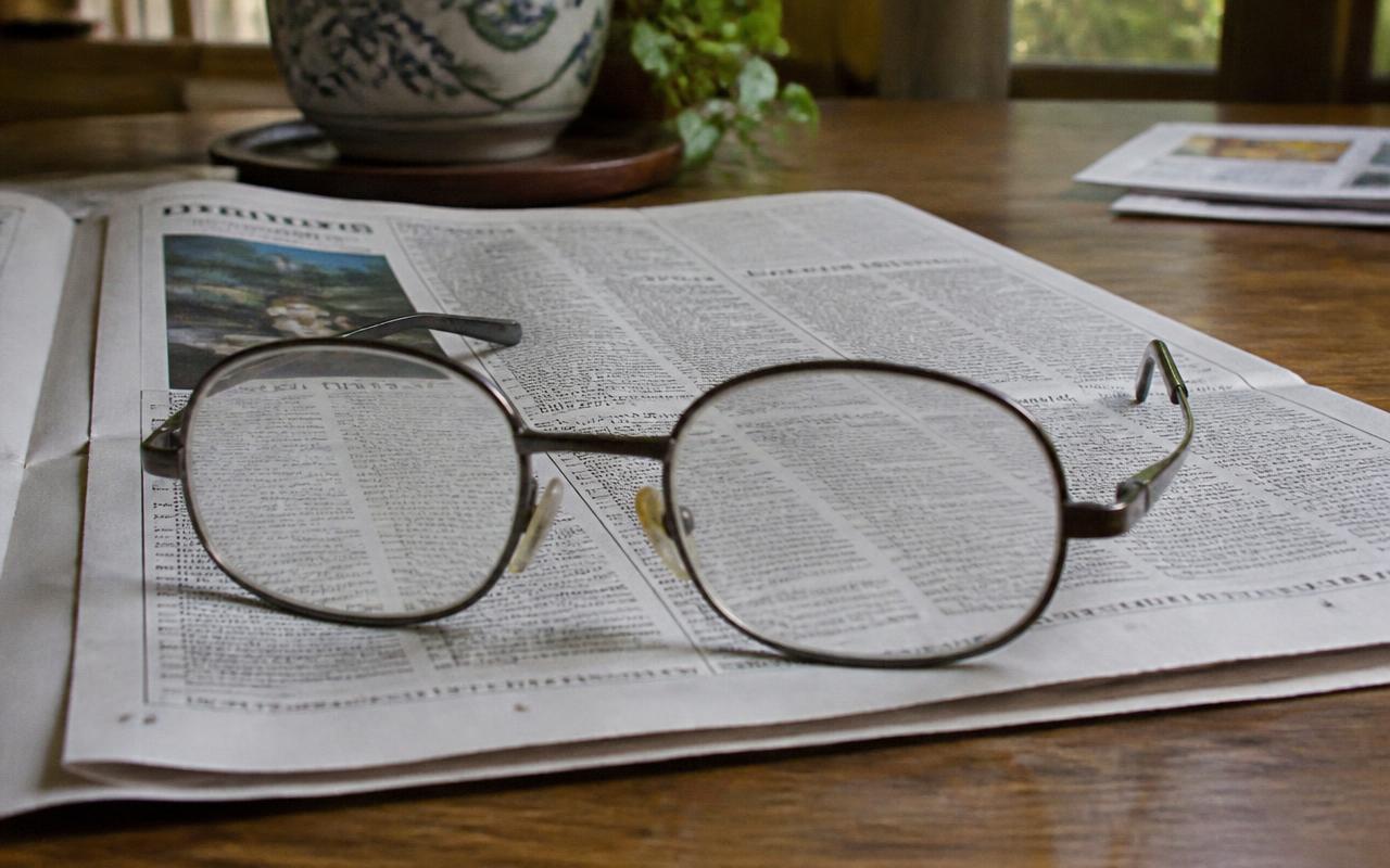 Óculos apoiado sobre um jornal aberto, com o texto embaçado através das lentes